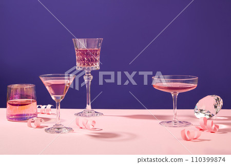 Several glasses filled with pink wine are decorated against purple background. Template with blank space for product advertising, celebration party concept 110399874