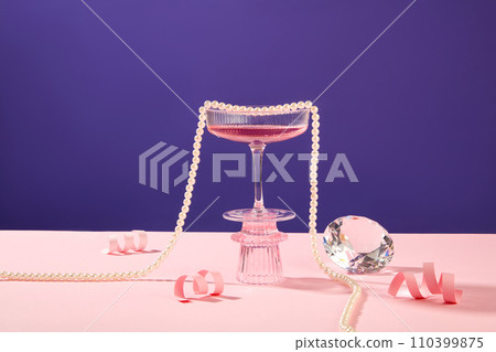 A glass of pink wine standing on a podium displayed with pink paper fireworks, a luxury diamond and a pearl necklace. New Year Party background greeting concept 110399875