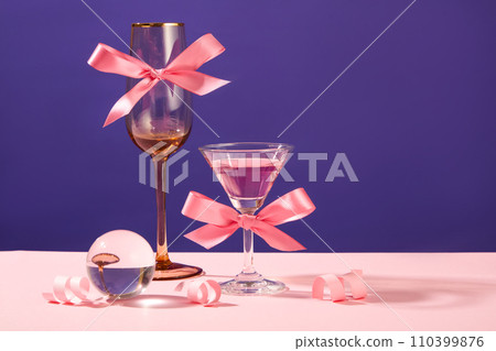 Women day, birthday or wedding party concept with two wine glasses decorated with pink bows. A glass ball and paper fireworks featured. Copy space 110399876