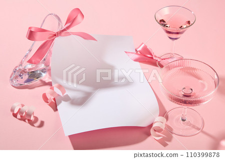 White paper with copy space surrounded by pink wine glasses, pink paper fireworks and two bows. A glass high heel featured. Valentine or birthday banner 110399878