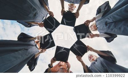 Graduates in black robes join their caps in a circle. Graduates in black robes join their caps in a circle. 110399922