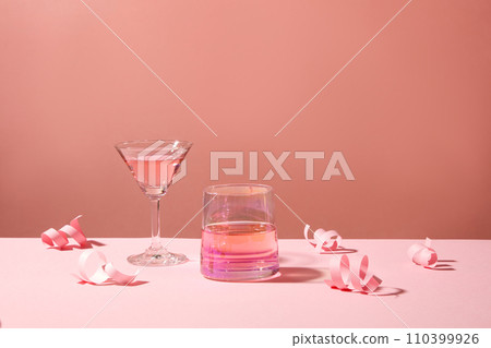 A cup and a cocktail glass decorated against pink background with paper fireworks. Concept of creative Christmas and New Year composition for template 110399926