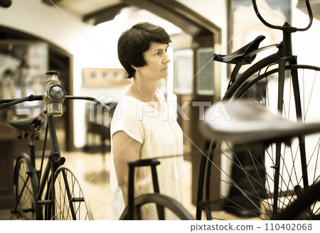 Mature woman examines the exhibit in museum 110402068