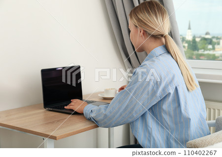 A woman with a cup of coffee is working on a laptop A woman with a cup of coffee is working on a laptop 110402267