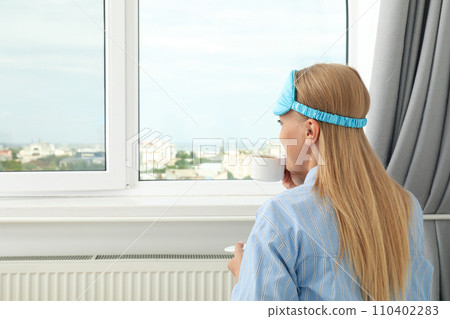 Young woman in sleeping mask drinking coffee in bed 110402283