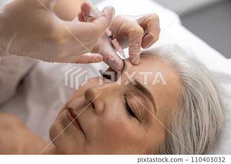 Beautician injecting filler into forehead of a female patient 110403032