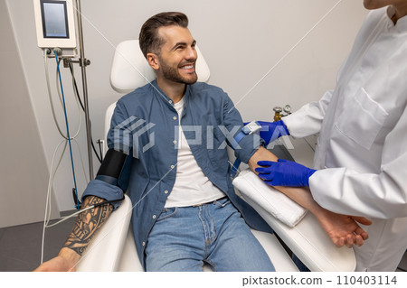 Smiling man preparing for insertion of drip in clinic. Smiling man preparing for insertion of drip in clinic. 110403114