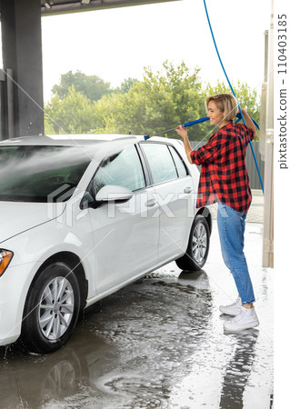 Woman in red shirt cleaning the car with a hose 110403185