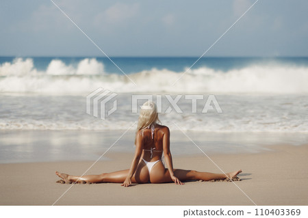 Tanned Bikini Beach Woman in Yoga Pose Doing Stretching Leg-split on Seashore 110403369