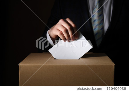 Paper box and hand with voting paper on dark background, close up 110404086