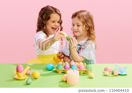 Happy smiling little girls, kids cracking painted Easter eggs, having fun against pink background. Positive mood. Easter, childhood 110404410