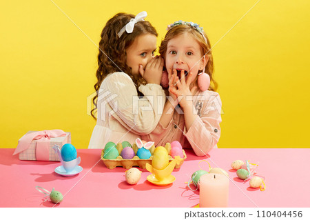 Little girl whispering to friend on ear, kids happy and excited face against yellow background. Easter, childhood 110404456