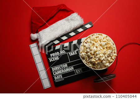 Reel, film, popcorn in paper cup, clapperboard and Santa's hat on red background, top view Reel, film, popcorn in paper cup, clapperboard and Santa's hat on red background, top view 110405044