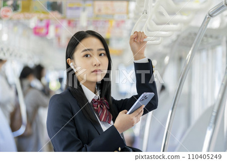 Image of a female high school student with a smart phone wearing earphones commuting to school by train 110405249