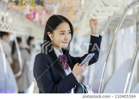 Image of a female high school student with a smart phone wearing earphones commuting to school by train 110405384