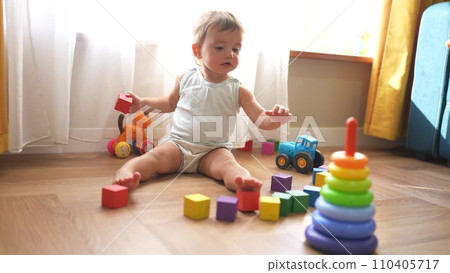 baby plays with toys cubes. kindergarten a teaching children kid dream concept. baby on the floor of the house plays with a pyramid lifestyle and cubes toys development of fine motor skills 110405717