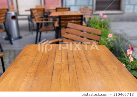Dining outdoors. Outdoor street cafe tables ready for service. Empty cafe terrace with wooden table and chair. Table of outdoor cafe on sidewalk with colorful plants and flowers Dining outdoors. Outdoor street cafe tables ready for service. Empty cafe terrace with wooden table and chair. Table of outdoor cafe on sidewalk with colorful plants and flowers 110405718