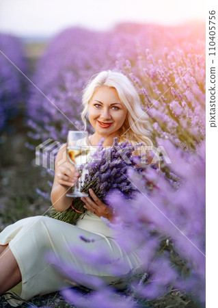 Blonde lavender field holds a glass of white wine in her hands. Happy woman in white dress enjoys lavender field picnic holding a large bouquet of lavender in her hands . Illustrating woman's picnic Blonde lavender field holds a glass of white wine in her hands. Happy woman in white dress enjoys lavender field picnic holding a large bouquet of lavender in her hands . Illustrating woman's picnic 110405756