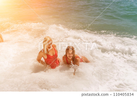 Women ocean play. Seaside, beach daytime, enjoying beach fun. Two women in red swimsuits enjoying themselves in the ocean waves. 110405834