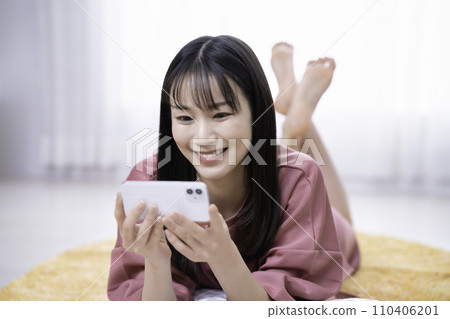 一位女士躺在地毯上觀看智能手機視頻 110406201