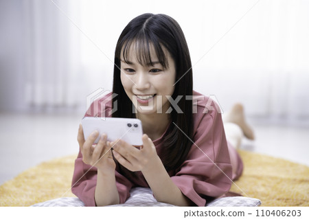 一位女士躺在地毯上觀看智能手機視頻 110406203