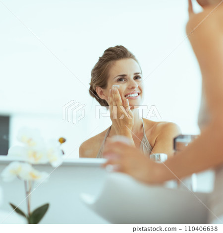 Happy young woman applying cream in bathroom 110406638