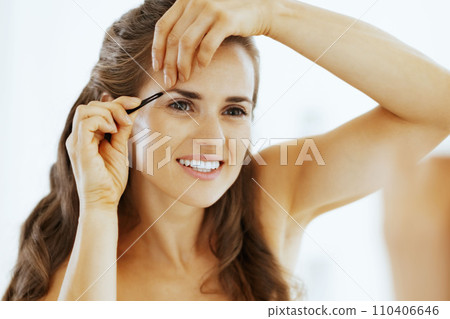 Happy young woman tweezing eyebrows Happy young woman tweezing eyebrows 110406646