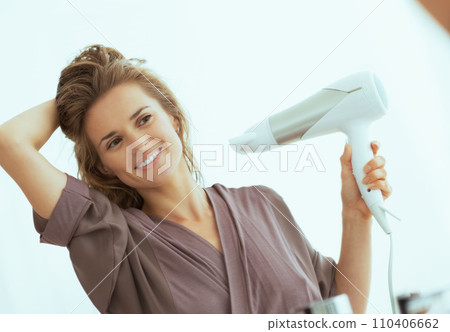 Happy young woman blow drying hair in bathroom 110406662