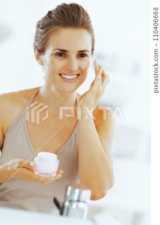 Smiling young woman applying cream in bathroom 110406668