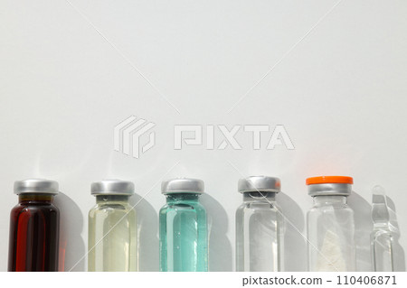 Glass medical bottles and ampoule with vaccine on white background, space for text 110406871