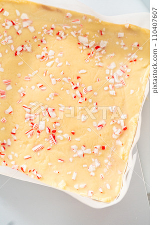Removing candy cane fudge from a square cheesecake pan lined with parchment. 110407607