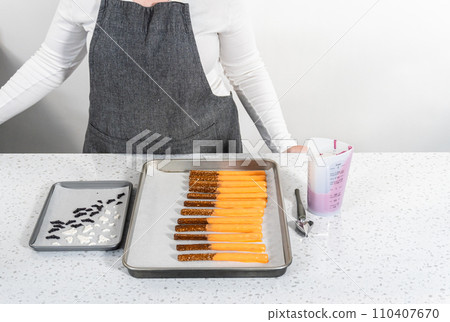 Dipping pretzel rods into melted chocolate to make Halloween chocolate-covered pretzel rods. 110407670