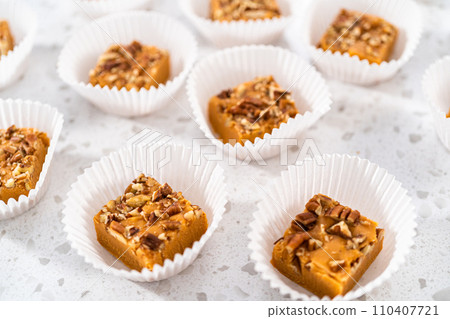 Homemade pumpkin spice fudge square pieces in white paper cupcake liners on a kitchen counter. 110407721