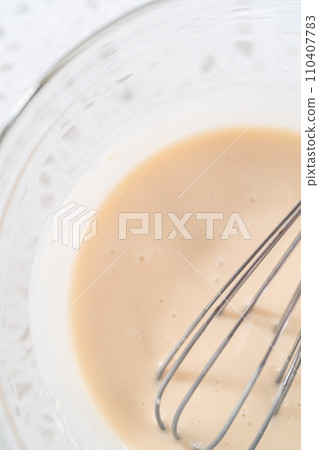 Mixing ingredients with a hand whisk in a glass mixing bowl to make the vanilla glaze. Mixing ingredients with a hand whisk in a glass mixing bowl to make the vanilla glaze. 110407783
