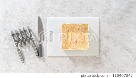 Flat lay. Removing candy cane fudge from a square cheesecake pan lined with parchment. Flat lay. Removing candy cane fudge from a square cheesecake pan lined with parchment. 110407842