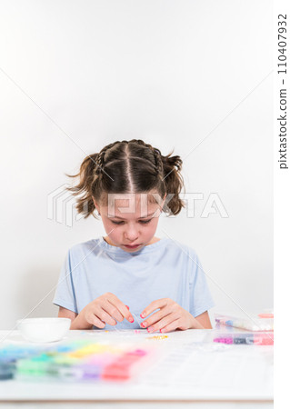 Little girl enjoys crafting colorful bracelets with vibrant clay beads set. Little girl enjoys crafting colorful bracelets with vibrant clay beads set. 110407932