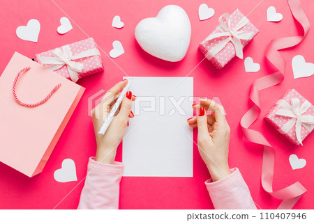 top view photo of valentine day decor female hands holding letter with envelope, small gift box and heart decoration on isolated pastel colored background with empty space 110407946