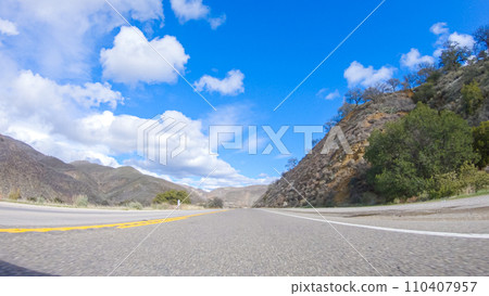 Vehicle is cruising along the Cuyama Highway under the bright sun. The surrounding landscape is illuminated by the radiant sunshine, creating a picturesque and inviting scene as the car travels 110407957