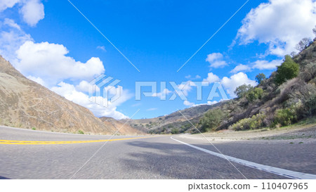 Vehicle is cruising along the Cuyama Highway under the bright sun. The surrounding landscape is illuminated by the radiant sunshine, creating a picturesque and inviting scene as the car travels 110407965