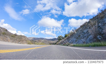 Vehicle is cruising along the Cuyama Highway under the bright sun. The surrounding landscape is illuminated by the radiant sunshine, creating a picturesque and inviting scene as the car travels 110407973