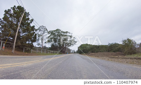 Vehicle navigates the streets of Morro Bay, California, during a cloudy winter day. The atmosphere is moody and serene as the overcast sky casts a soft light on the charming buildings and quiet 110407974