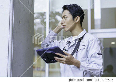 一名穿著工作服的年輕人一邊查看平板電腦一邊檢查建築物。照片由有明教育藝術學院提供。 110408687