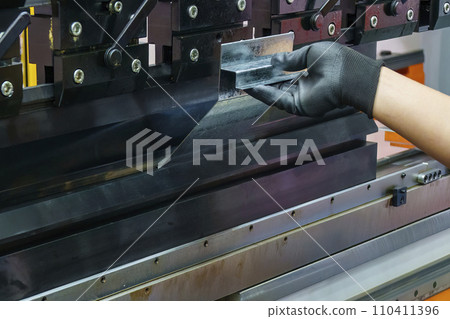 Close up the bending machine operator hold the sheet metal parts with rubber glove. Close up the bending machine operator hold the sheet metal parts with rubber glove. 110411396