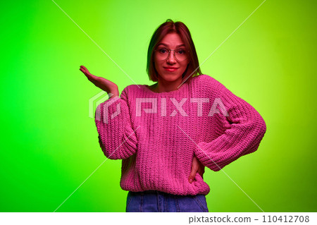 Young emotional girl in fashion glasses and raising hand of surprise and looking at camera against green gradient studio background. Young emotional girl in fashion glasses and raising hand of surprise and looking at camera against green gradient studio background. 110412708
