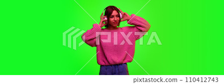 Banner. Young beautiful girl posing puts headphones on head against green studio background with negative space to insert text. 110412743