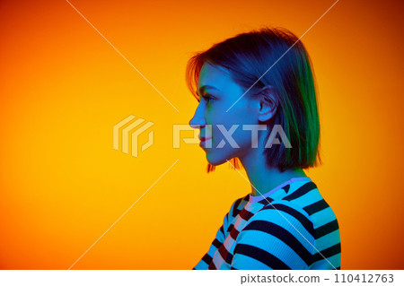 Profile view portrait of young attractive girl with short hair against gradient orange background with negative space to insert text. Profile view portrait of young attractive girl with short hair against gradient orange background with negative space to insert text. 110412763