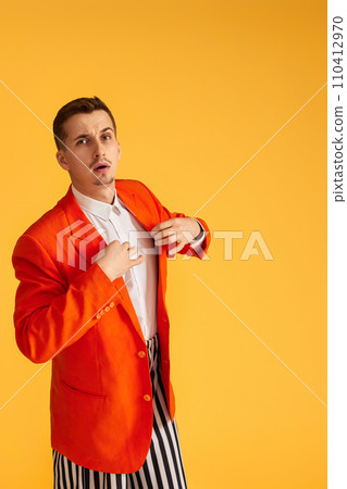 extravagant young man in orange jacket and striped pants on yellow background. extravagant young man in orange jacket and striped pants on yellow background. 110412970