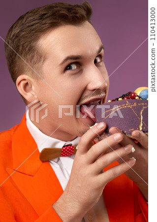 handsome birthday man in orange jacket eating cake on purple background. joy, fun handsome birthday man in orange jacket eating cake on purple background. joy, fun 110413000
