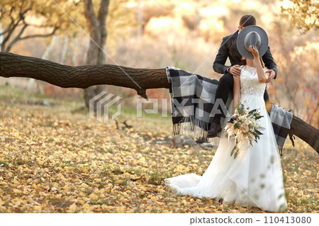 beautiful happy stylish bride and groom kissing and covering by hat outdoor in autumn 110413080