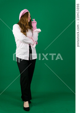 full-length woman in black pants, shoes and a pink shirt, winter gloves and a beret on her head on a green background, standing in thought, crossing her fingers on her left hand, long hair full-length woman in black pants, shoes and a pink shirt, winter gloves and a beret on her head on a green background, standing in thought, crossing her fingers on her left hand, long hair 110413898